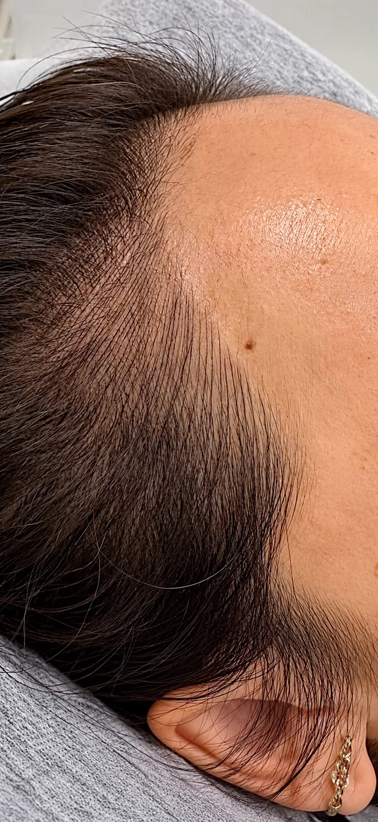 A woman's hairline and temple from the side, hair strokes blending into longer dark hair